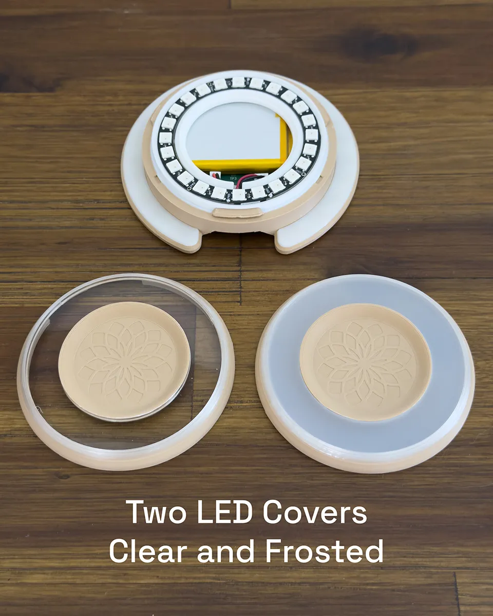 The Aura Light with its LED ring exposed, shown with both twist-on covers — clear and frosted — resting in front of it on a wood table
